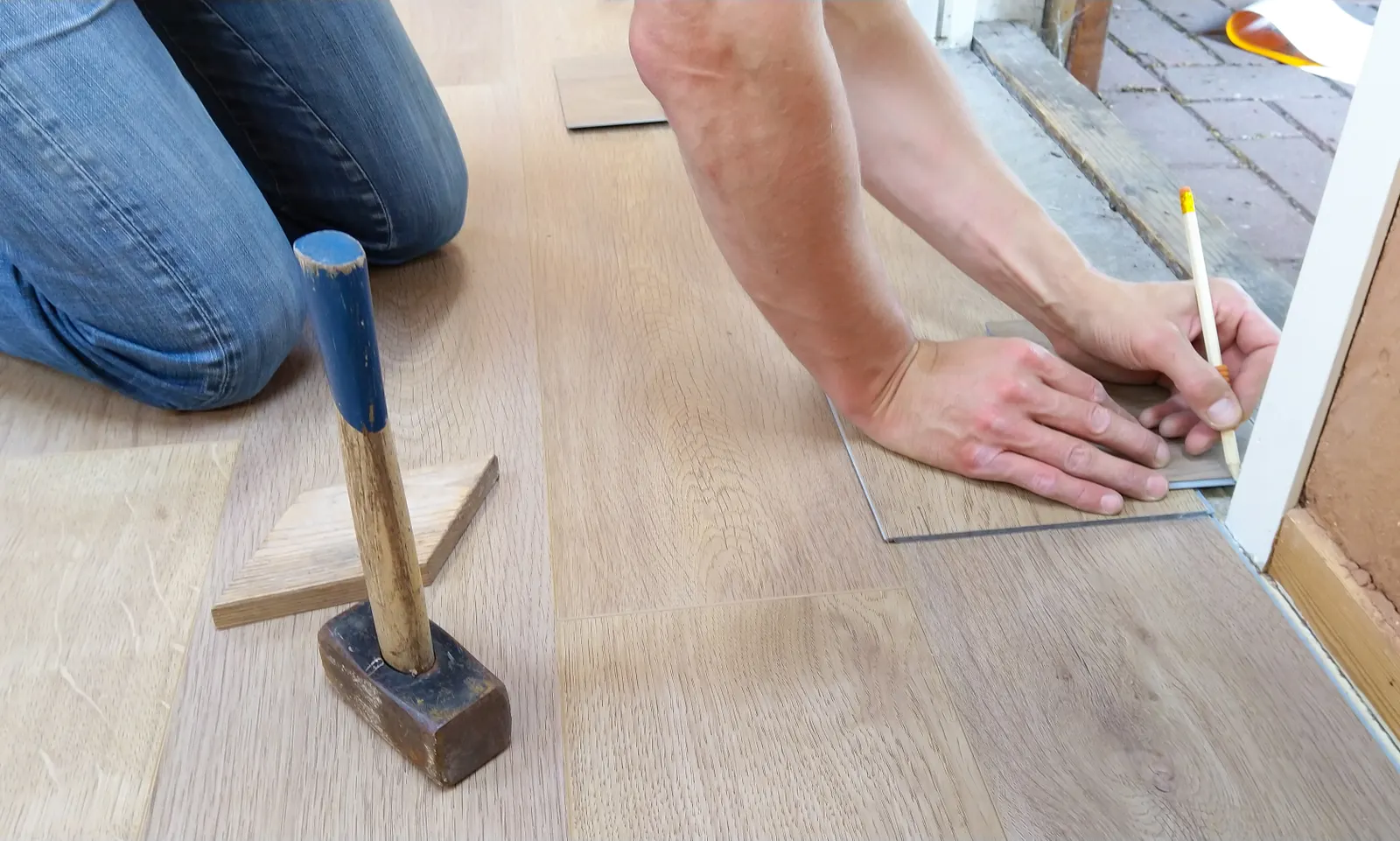 Leerer Raum mit fertig verlegtem Holzoptik-Boden, weißen Sockelleisten in einem Karton und einem Besen