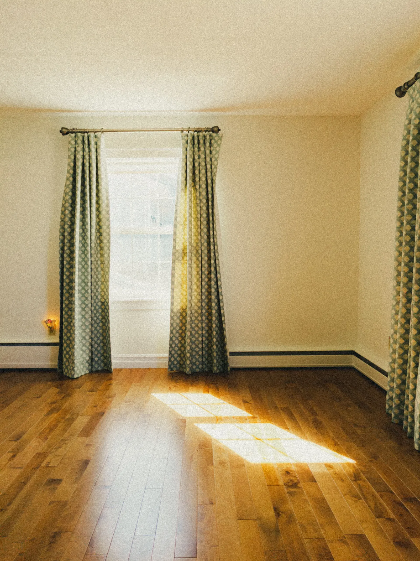 Leeres Zimmer mit Dielenboden, durch das Fenster fällt ein scharf begrenztes Rechteck Sonnenlicht auf den Boden