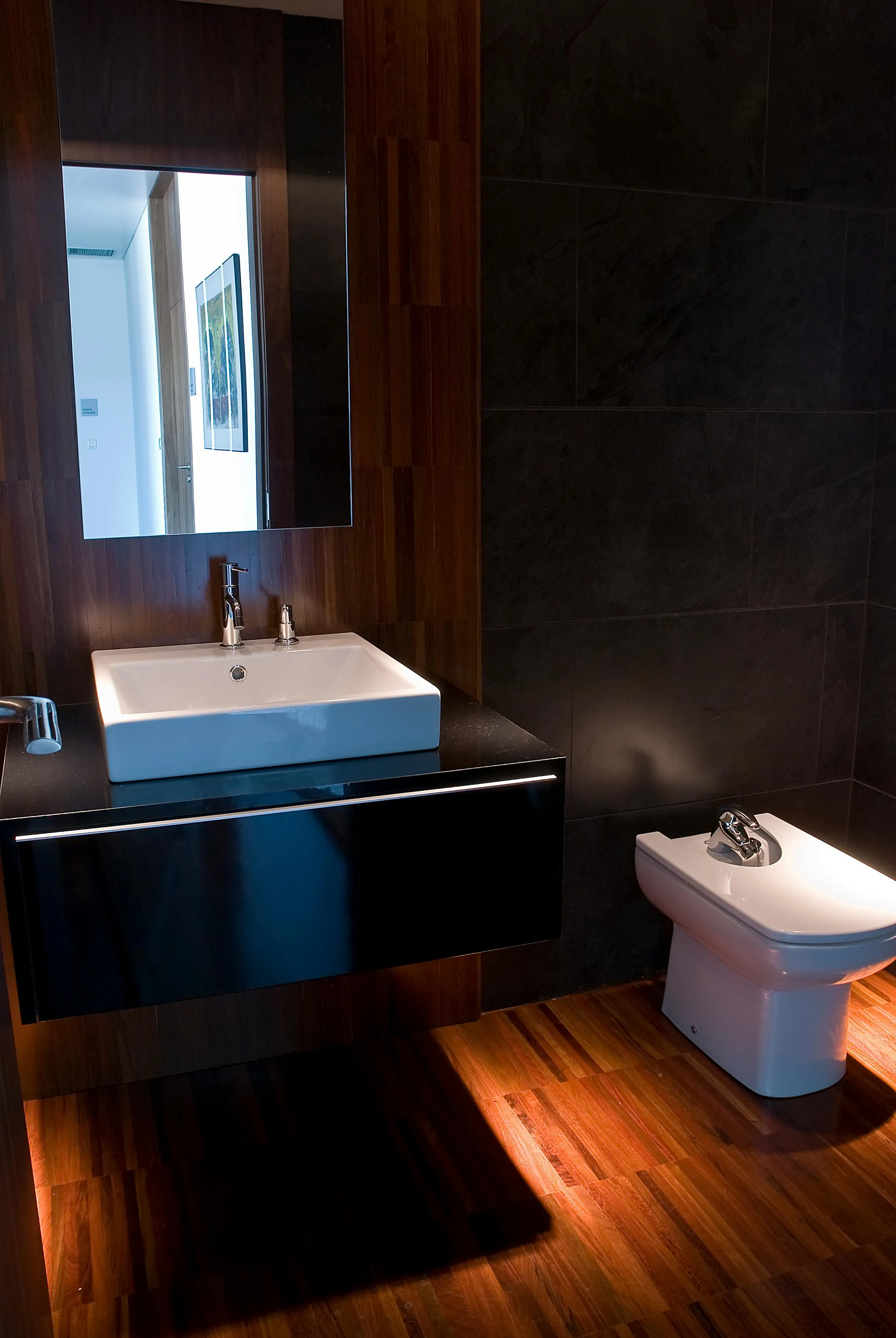 Modernes Wohnbad in dunkler Optik mit warmem Vinylboden in Holzoptik, Waschtisch und Bidet ohne Dusche
